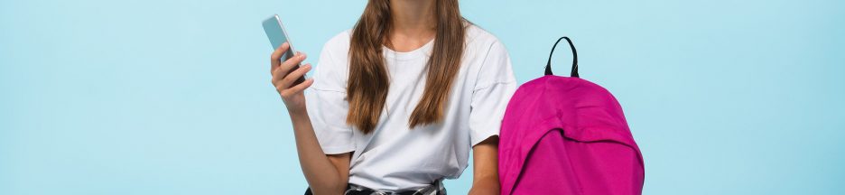 podcast-therapie-jeunes-français Jeune fille à côté d’un cartable rose casque blanc sur les oreilles et smartphone dans une main