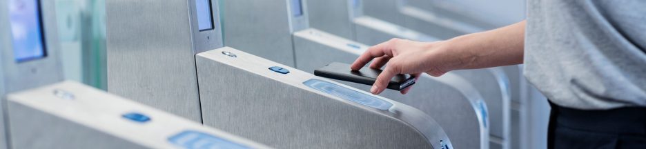 Une femme devant le portique d’une station de métro présentant son passe navigo sur iPhone.