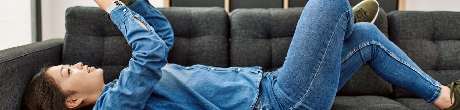 Une jeune femme sur un sofa, en train d’écrire un message écrit sur son smartphone, SMS ou message en ligne.