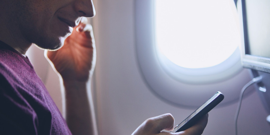 Un homme en train de manipuler son smartphone et éventuellement, d’en activer le mode avion.
