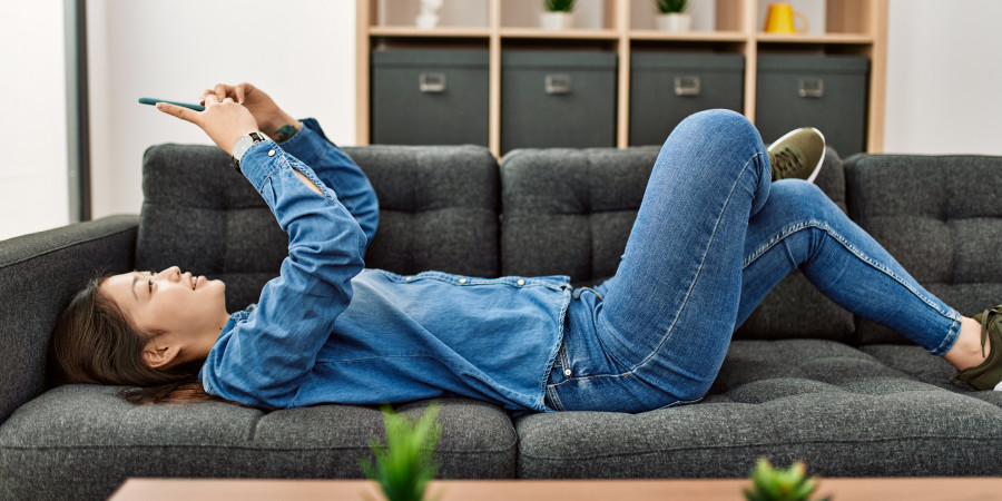 Une jeune femme allongée sur un sofa et en train de lire des textes de formats Notes sur les réseaux sociaux.