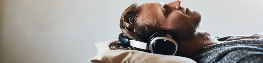 Un homme allongé sur son lit, casque aux oreilles et en train d’écouter des bruits pour s’endormir.