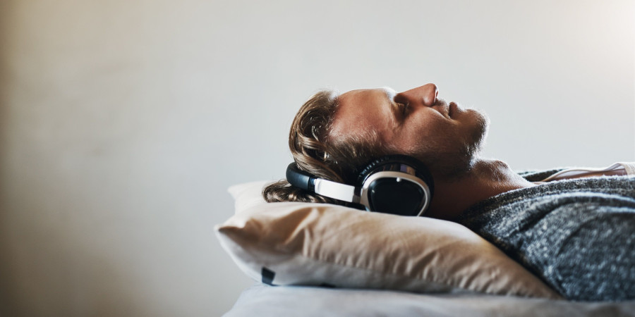 Un homme allongé sur son lit, casque aux oreilles et en train d’écouter des bruits pour s’endormir.
