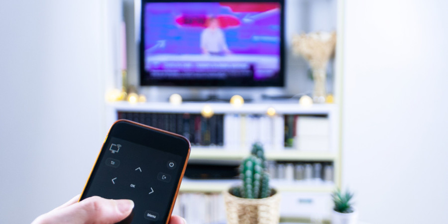 Un smartphone servant de télécommande TV pour un téléviseur connecté installé dans un salon.