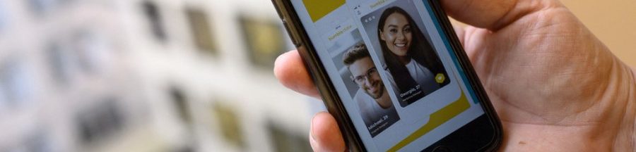 Une personne tenant son smartphone, en train de consulter le profil de rencontre deux personnes pour voir s’ils sont taxés « beige flag ».