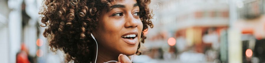 Une jeune femme dans la rue en train de discuter à travers un kit mains libres pour éviter les risques d’exposition aux ondes émises par un smartphone.