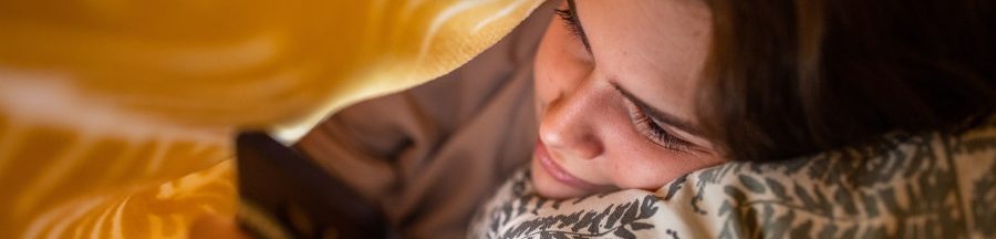 dependance-a-internet-profils-internautes Une jeune adolescente ayant une dépendance à Internet, cachée sous sa couverture, qui surfe en ligne sur son smartphone.