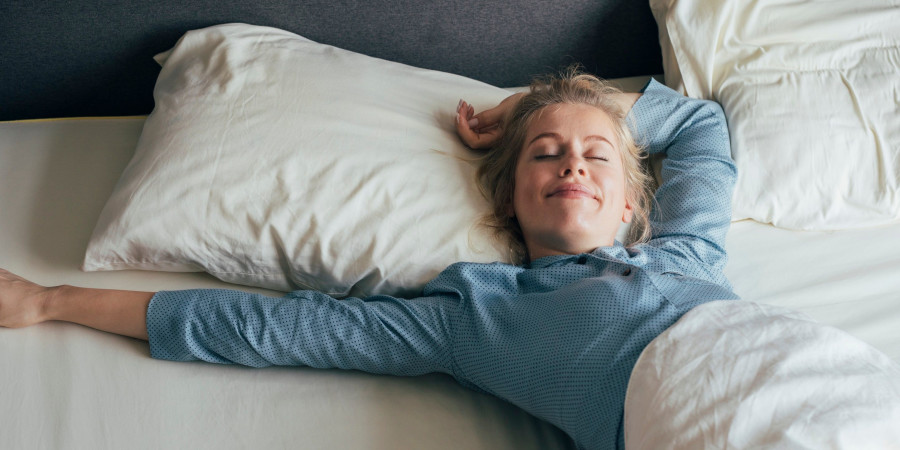 Une femme dans son lit, profitant des quelques minutes de répit accordées par la répétition d’alarme de la fonction snooze de son réveil.
