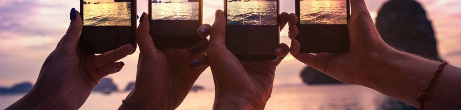 Des vacanciers au bord de la plage en train de prendre des photos sur smartphone.