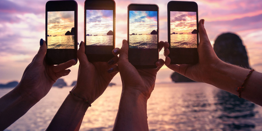 Des vacanciers au bord de la plage en train de prendre des photos sur smartphone.