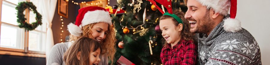 Une famille de quatre, assise devant leur sapin de Noël, en train de s’offrir des cadeaux high-tech écolos.