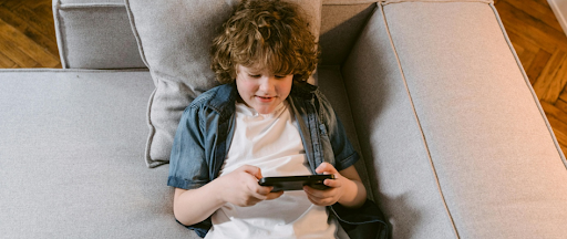 Un jeune garçon allongé sur un canapé blanc, jouant sur un smartphone. Un jeune garçon allongé sur un canapé blanc, jouant sur un smartphone.