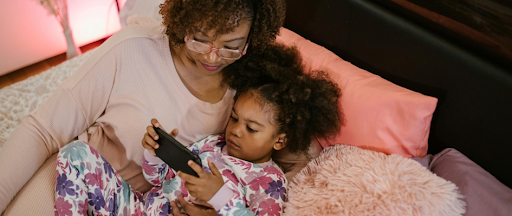 Une mère avec sa fille au lit, jouant à un jeu sur smartphone. Une mère avec sa fille au lit, jouant à un jeu sur smartphone.
