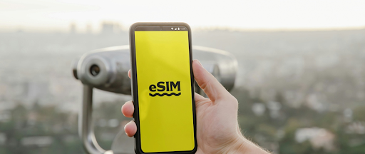 Une personne tenant un smartphone affichant le logo de l’eSIM sur un fond jaune. Une personne tenant un smartphone affichant le logo de l’eSIM sur un fond jaune.