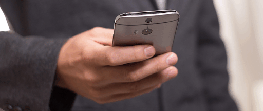 Un homme en costume complet tenant dans sa main un smartphone gris.