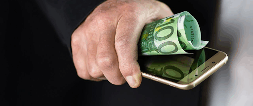 Un homme tenant dans la main un smartphone et un billet de banque. Un homme tenant dans la main un smartphone et un billet de banque.