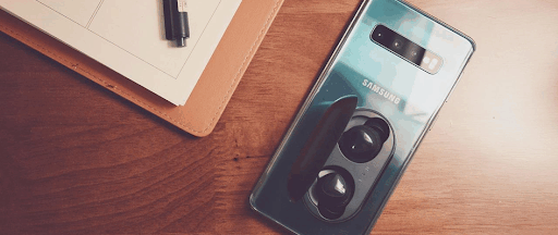 Un smartphone Samsung et des Galaxy Airbuds posés à côté d’une pile de documents.