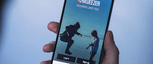 Une main tenant un smartphone avec l’application mobile Deezer ouverte. Une main tenant un smartphone avec l’application mobile Deezer ouverte.