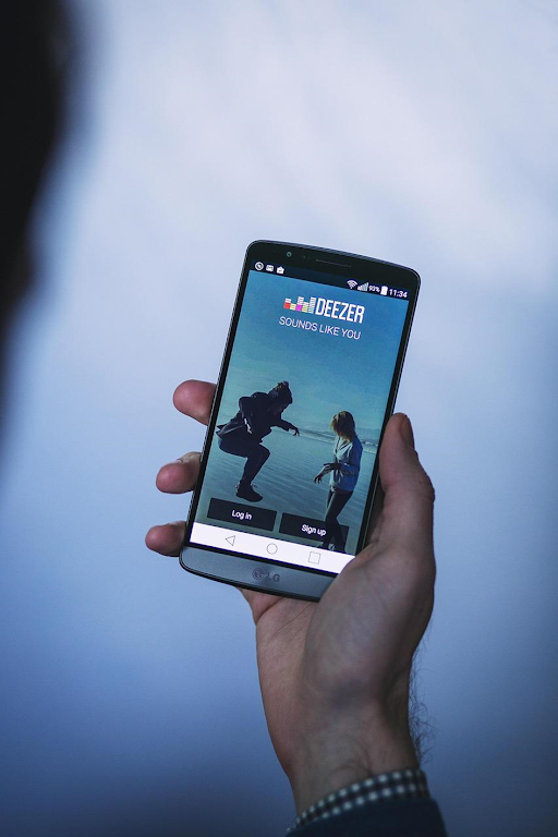 Une main tenant un smartphone avec l’application mobile Deezer ouverte.