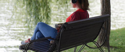 Une femme assise au bord de l’eau sur un banc public, coiffée d’un casque audio.