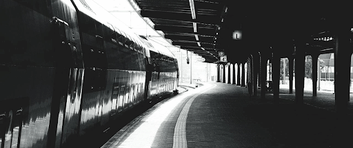 Une image en noir et blanc d’un quai de gare avec un train qui passe.