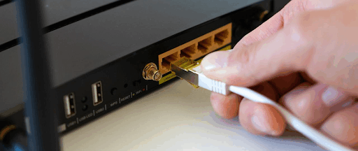 Une main sur le point de brancher une prise Ethernet à une box internet.