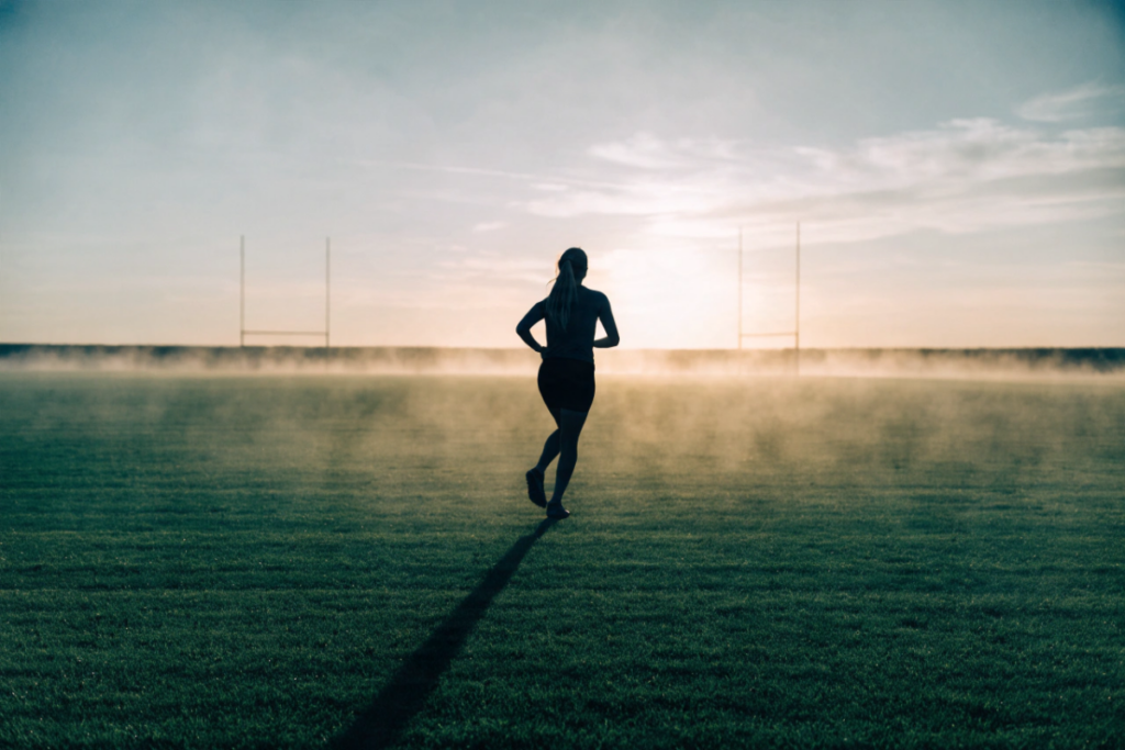 Silhouette de joueuse de football s'échauffant seule sur un terrain vide