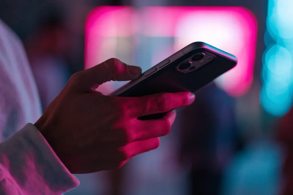 une main tient un smartphone qui filme une scène éclairée par des néons colorés évoquant Rosé de BLACKPINK