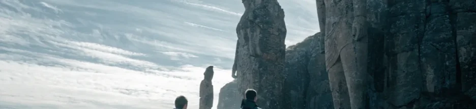 deux hommes en imperméable regardant des statues monumentales évoquant le film Wild Horse Nine
