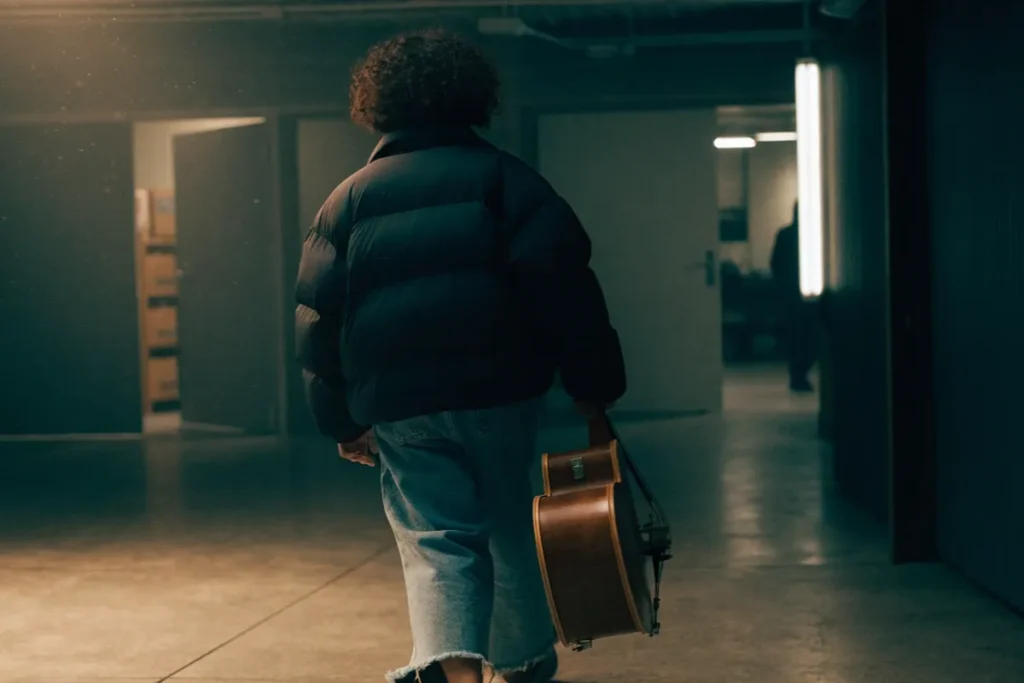 musicien entrant dans les coulisses avec un étui de violoncelle rappelant Behemoth